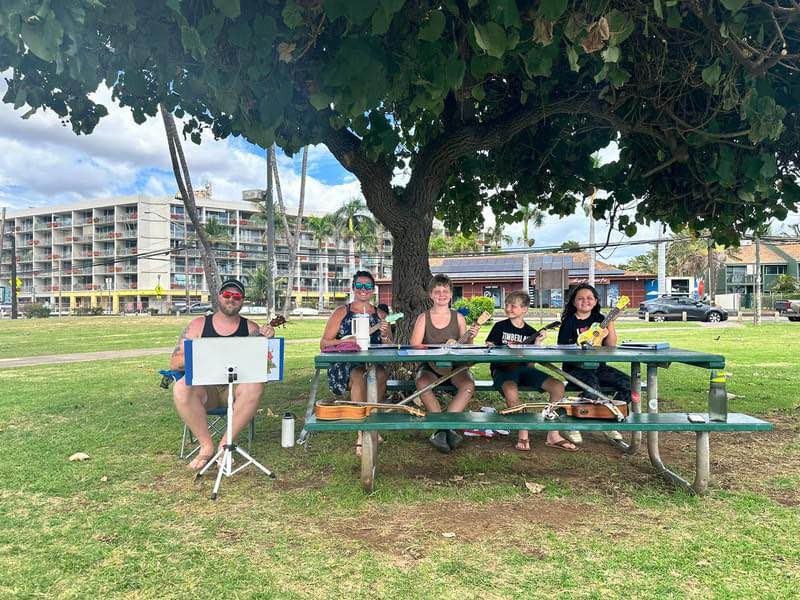 Student learning ukulele on a peaceful Maui beach with ocean waves in background